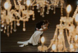 Jack 10 | The Heritage Centre by Mountain View Events Ltd. A groom kissing his bride as he gracefully dips her in a dance-style pose beneath stunning chandeliers at a country wedding venue near Calgary, Alberta. The romantic moment is framed by the venue's elegant and rustic charm.