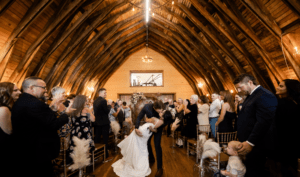 Ceremony-Kiss | The Heritage Centre by Mountain View Events Ltd. The groom gently kisses his bride in a rustic barn ceremony space, surrounded by warm, country-themed decor at their intimate wedding