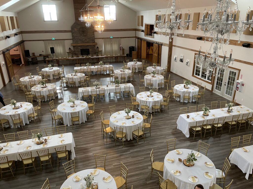 A ballroom at a country event venue near Calgary, Alberta, featuring elegantly arranged tables, a majestic stone fireplace as the centerpiece, and rustic wooden accents creating a warm and sophisticated atmosphere