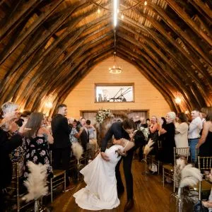 Groom kissing his bride inside a historic barn, surrounded by rustic wooden beams and a romantic, intimate atmosphere