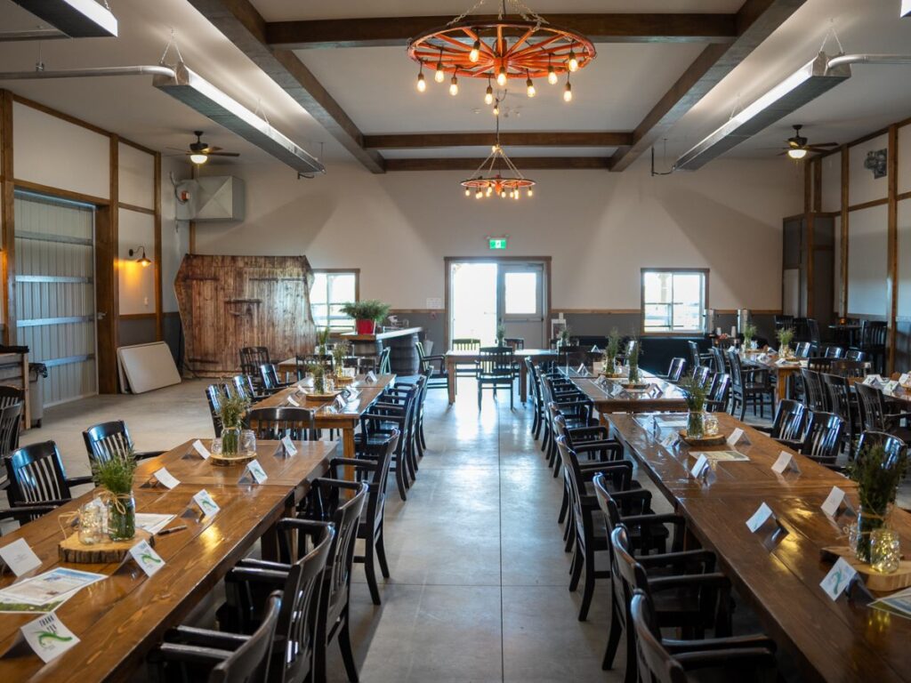 Country event venue near Calgary, Alberta, showcasing beautiful wooden tables custom chandeliers casting warm light, and rustic charm enhanced by exposed wooden beams and natural décor.