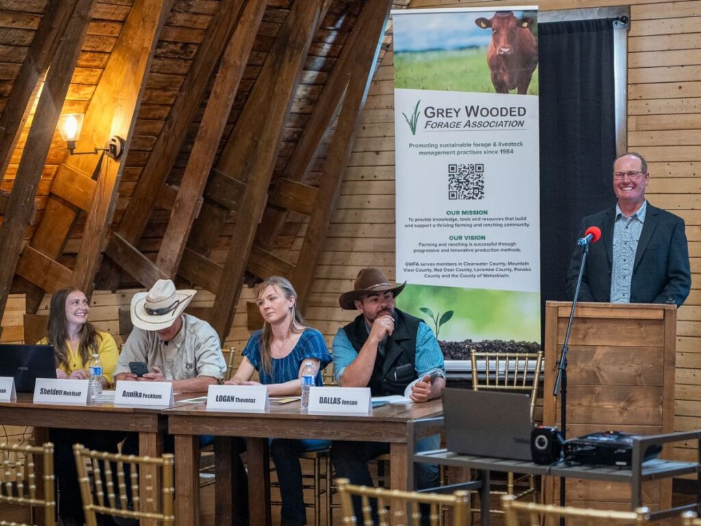 Participants listening intently to a presentation in a historic barn meeting room at a country event venue near Calgary, featuring rustic wooden beams, vintage decor, and warm natural lighting creating an inviting atmosphere