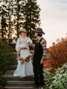 Bride and groom wearing cowboy hats on an outdoor staircase at a rustic country wedding venue, surrounded by picturesque countryside.