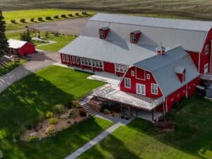 Aerial view of a stunning large red barn nestled in the picturesque countryside, surrounded by lush green fields and rolling hills.