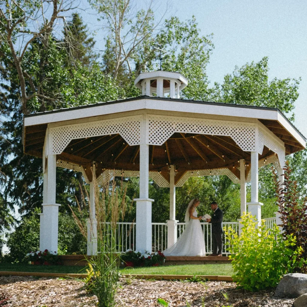 ride and groom standing together in a beautiful white gazebo, surrounded by lush greenery at a picturesque country wedding venue