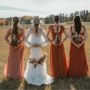 Bride wearing a cowboy hat standing with her bridesmaids at a beautiful country wedding venue, surrounded by vibrant fall colors and rustic charm."