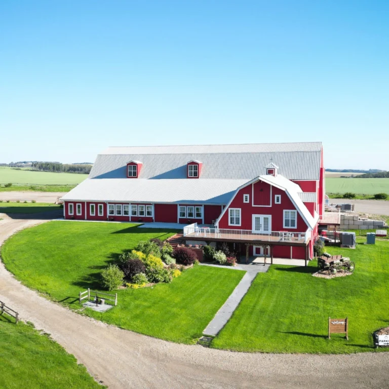Aerial view of a red barn wedding venue with green lawns, gardens, and countryside surroundings.