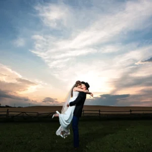 Groom in a cowboy hat lifts his bride for a sunset kiss in the open fields at The Heritage Centre country wedding venue in Alberta.