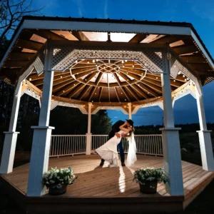 Night Portraits at the White Gazebo – The Heritage Centre | The Heritage Centre by Mountain View Events Ltd. | The Heritage Centre by Mountain View Events Ltd. Couple kisses under a lit gazebo at night with string lights and a deep blue sky.