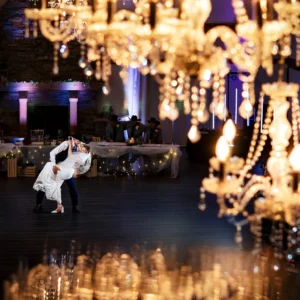 Couple dances in a dim ballroom while crystal chandeliers sparkle in the foreground.