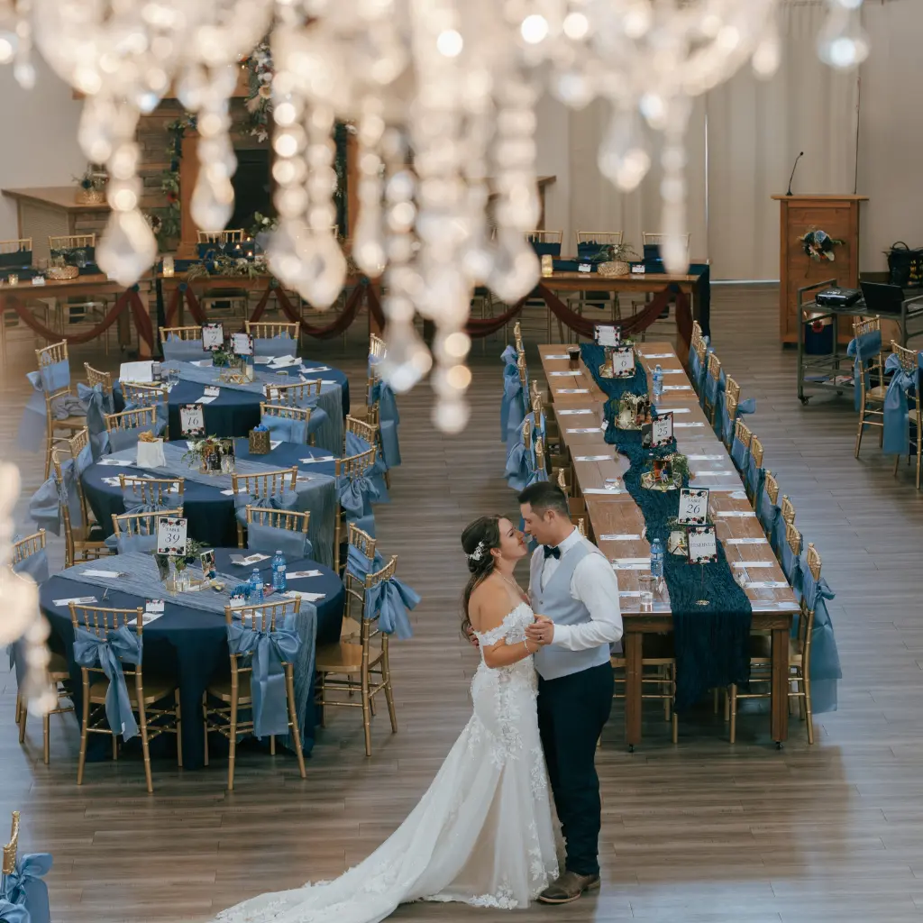 Bride and groom share their first dance in The Heritage Centre ballroom beneath crystal chandeliers and surrounded by blue wedding décor.