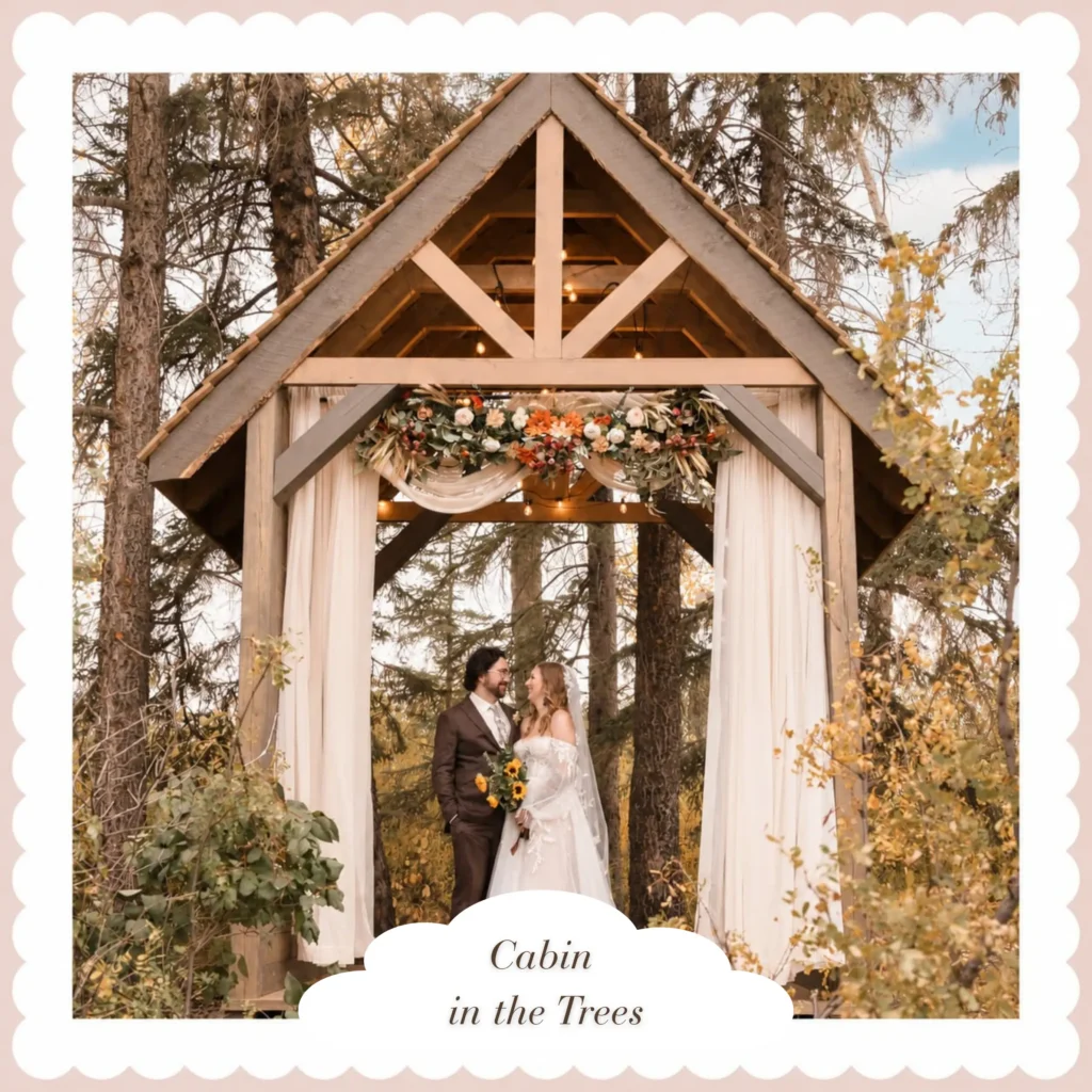 Wedding couple standing beneath the flower-decorated Cabin in the Trees ceremony structure surrounded by autumn foliage.