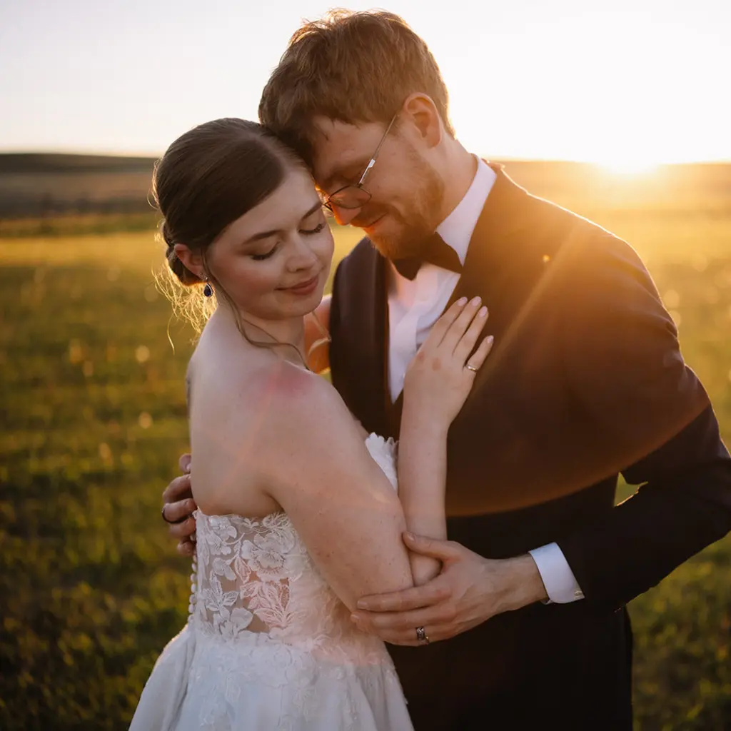 Newlywed couple embracing in a sunlit field during golden hour at The Heritage Centre wedding venue in Alberta.