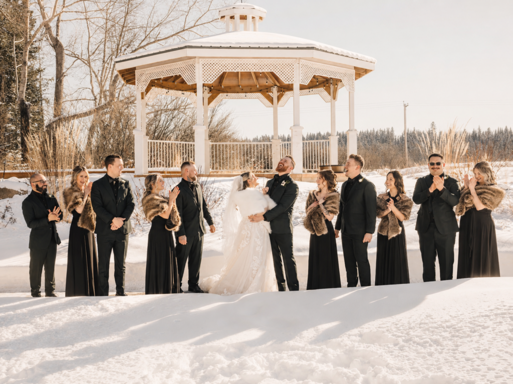 Brittany and Avery laugh with their wedding party in the snow in front of the white gazebo at The Heritage Centre.