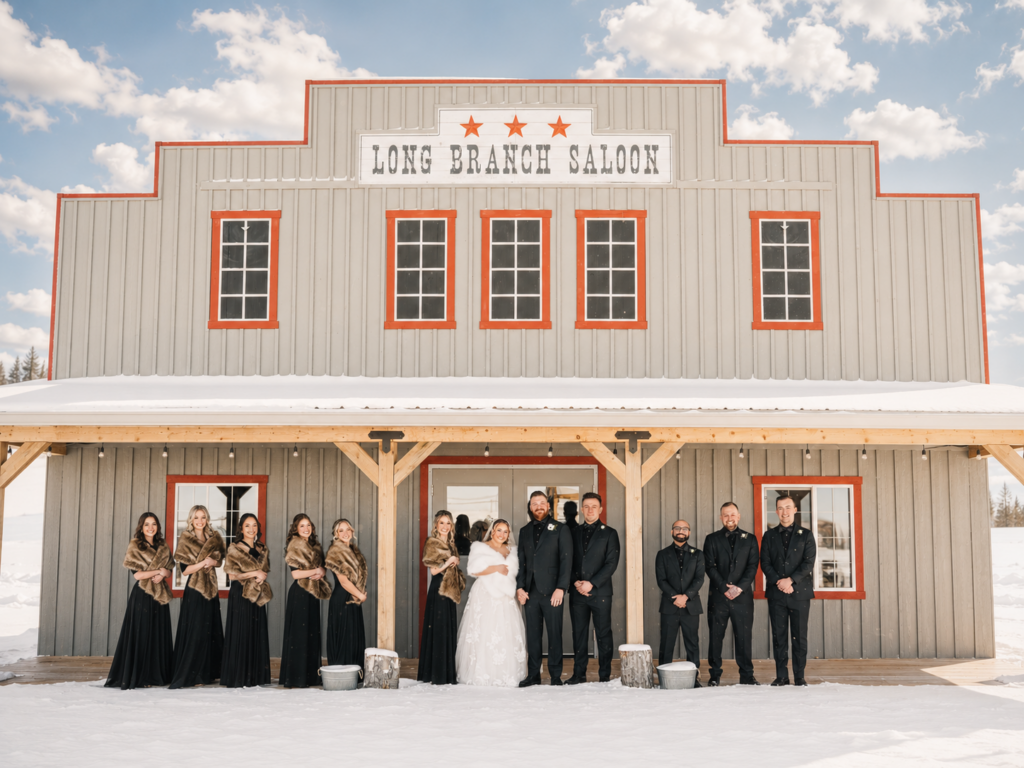 Long Branch Saloon Winter Wedding Party | The Heritage Centre by Mountain View Events Ltd. | The Heritage Centre by Mountain View Events Ltd. Winter wedding party poses in the snow outside the Long Branch Saloon at The Heritage Centre in Cremona, Alberta.