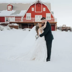 Newlywed couple embracing in the snow outside the red barn at The Heritage Centre in Alberta.