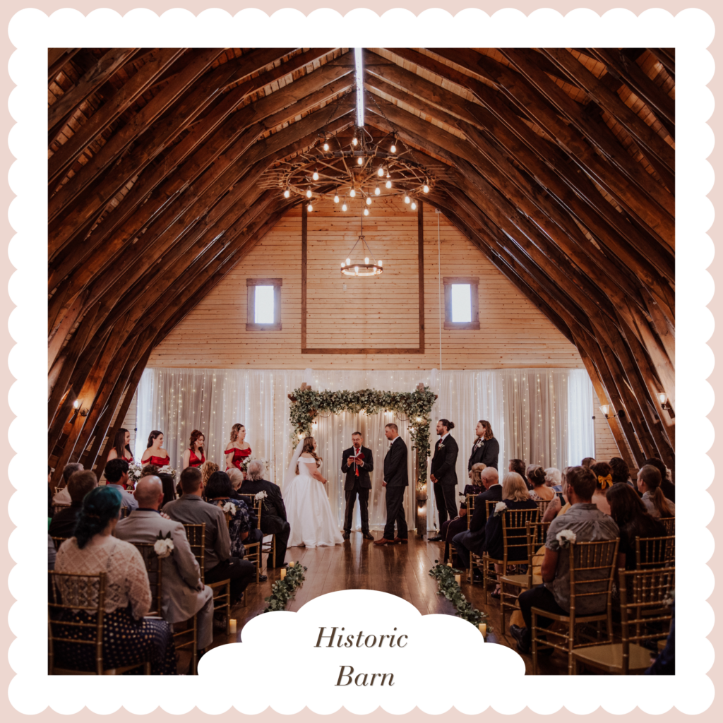Historic Barn Ceremony Venue | The Heritage Centre by Mountain View Events Ltd. | The Heritage Centre by Mountain View Events Ltd. Wedding ceremony in a historic barn with a wooden arched ceiling, chandeliers, and vines framing the officiant and couple at the altar.