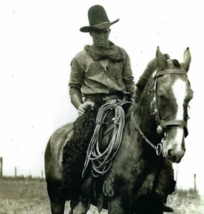 Black and white vintage photo of Russell Rice on horseback with a coiled lasso, taken on the family farm near Torrington, Alberta