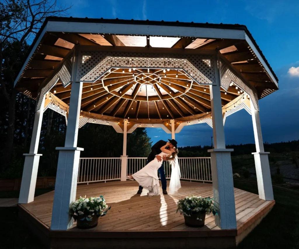 Couple sharing a kiss beneath the glowing white gazebo at twilight at The Heritage Centre, a wedding venue near Calgary