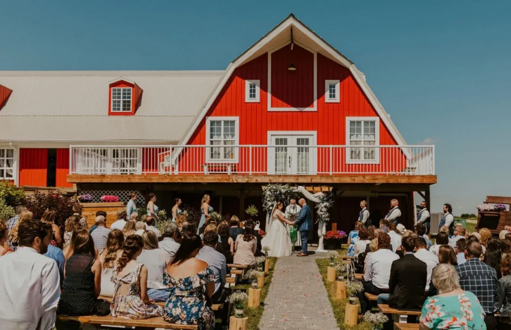 Outdoor wedding ceremony with guests seated in front of The Heritage Centre red barn.